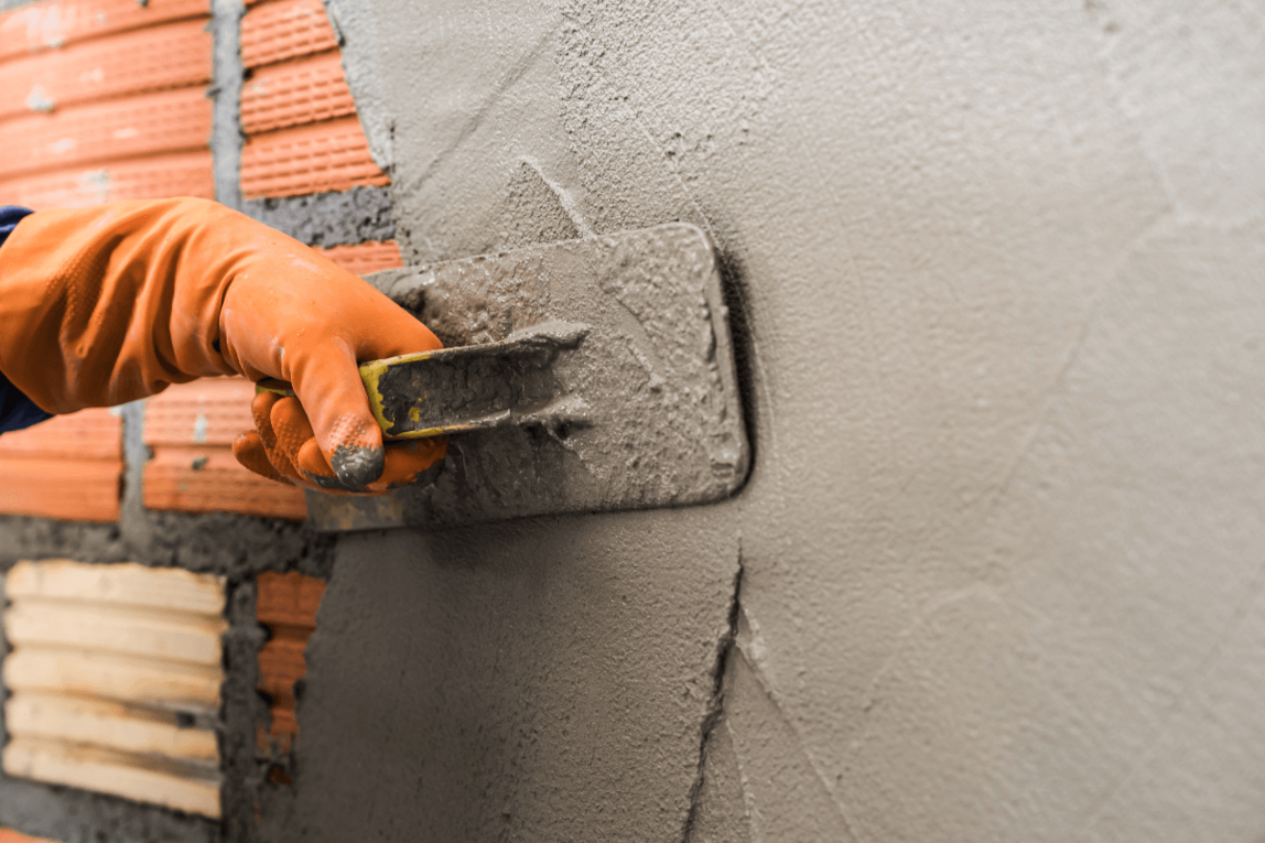 Eine Hand, die mit einem Spachtel eine Wand verputzt.